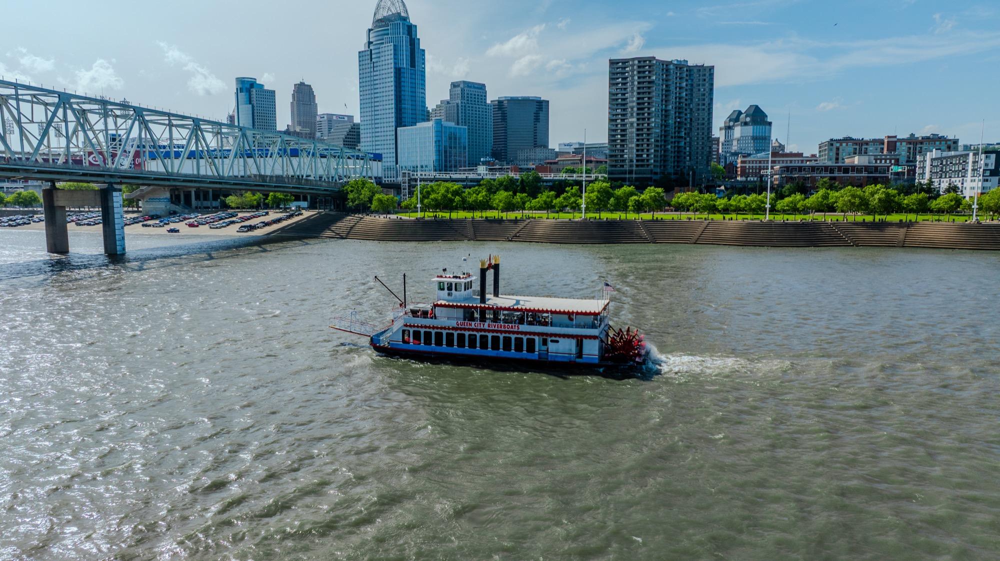 A Queen City Riverboats paddlewheeler on the Ohio River passing the Cincinnati riverfront and Great American Ball Park