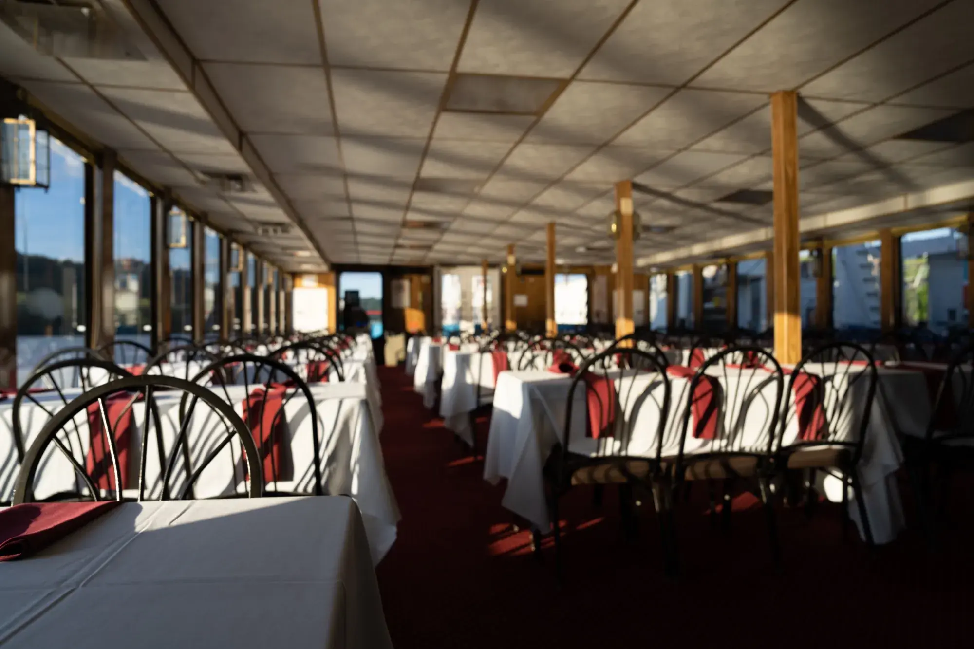 An enclosed dining deck set with white linens and red napkins before guests board